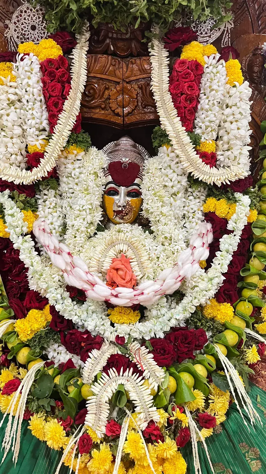 ಬಿಳಿ ಮತ್ತು ಕೆಂಪು ಹೂವುಗಳ ಹಲವು ಸುತ್ತಿನ ಹಾರಗಳಿಂದ ಅಲಂಕೃತಳಾದ ದೇವಿ
