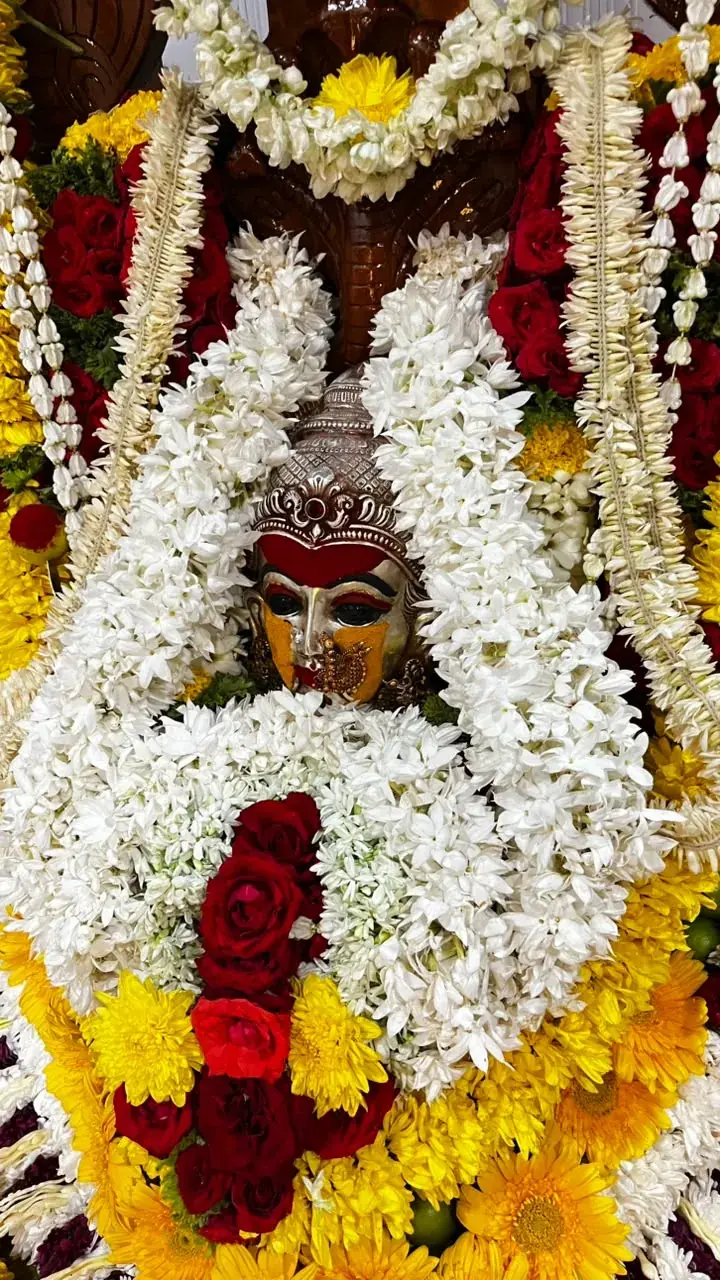 ಮಲ್ಲಿಗೆ ದಂಡೆ, ಕೆಂಪು ಗುಲಾಬಿ ಮತ್ತು ಹಳದಿ ಸೇವಂತಿಗೆಗಳ ನಡುವೆ ಕುಂಕುಮ ಮತ್ತು ಅರಿಶಿನದಿಂದ ಕೂಡಿದ ದೇವಿ ಅಮ್ಮನವರ ಬೆಳ್ಳಿಯ ಮುಖವಾಡದ ಹತ್ತಿರದ ನೋಟ