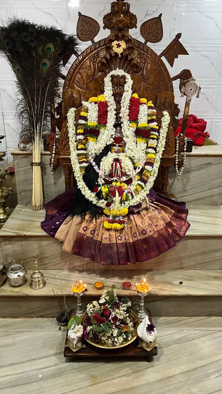 ನವಿಲುಗರಿಗಳ ನಡುವೆ ಕೆತ್ತನೆಯ ಮರದ ಪ್ರಭಾವಳಿಯ ಮುಂದೆ ಅಮ್ಮನವರು