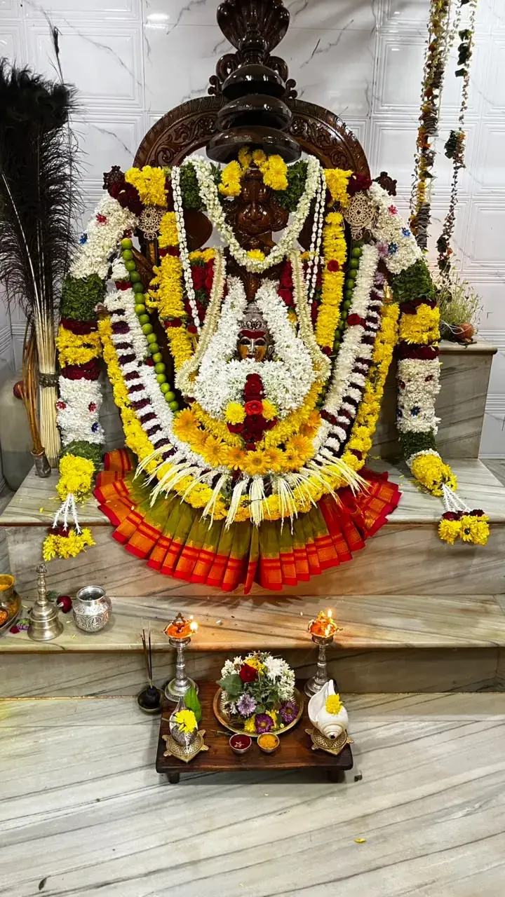 ಹಳದಿ ಸೇವಂತಿಗೆ, ಮಲ್ಲಿಗೆ ಮತ್ತು ಕೆಂಪು ಗುಲಾಬಿಗಳ ಸಂಪೂರ್ಣ ಅಲಂಕಾರದಲ್ಲಿ, ಕಿತ್ತಳೆ ಮತ್ತು ಹಸಿರು ರೇಷ್ಮೆ ಸೀರೆ ಉಟ್ಟು ಕೆತ್ತನೆಯ ಸಿಂಹಾಸನದಲ್ಲಿರುವ ದೇವಿ ಅಮ್ಮನವರು, ಮುಂದೆ ಎರಡು ದೀಪಗಳು