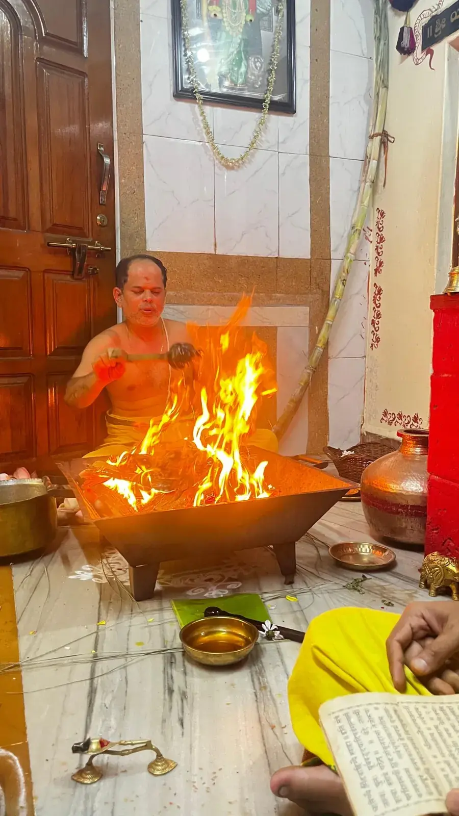 ಭಕ್ತರೊಬ್ಬರು ಪವಿತ್ರ ಗ್ರಂಥ ಪಠಿಸುತ್ತಿರುವಾಗ ಉದ್ದನೆಯ ಸೌಟಿನಿಂದ ಉರಿಯುತ್ತಿರುವ ಹೋಮದ ಅಗ್ನಿಗೆ ತುಪ್ಪ ಅರ್ಪಿಸುತ್ತಿರುವ ಅರ್ಚಕರು