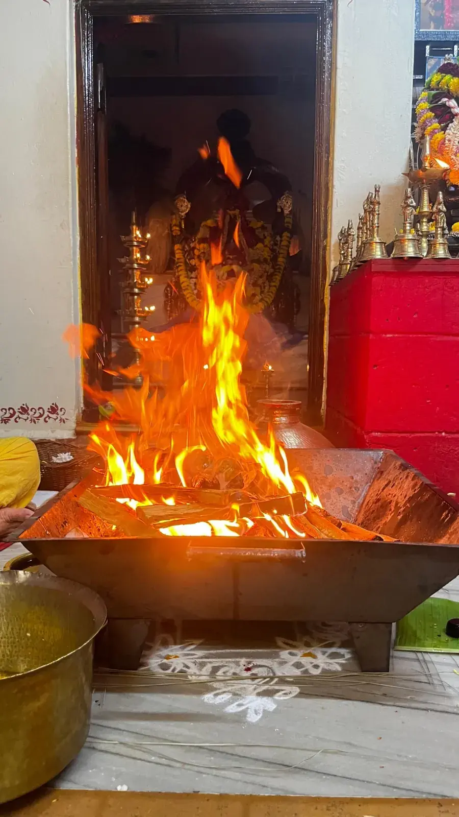 ತೆರೆದ ಗರ್ಭಗುಡಿಯ ಬಾಗಿಲಿನ ಮುಂದೆ ಏರುತ್ತಿರುವ ಹೋಮದ ಜ್ವಾಲೆಗಳು, ಒಳಗೆ ದೇವಿ ಅಮ್ಮನವರು ಮತ್ತು ಬೆಳಗುತ್ತಿರುವ ಹಿತ್ತಾಳೆ ದೀಪಗಳು