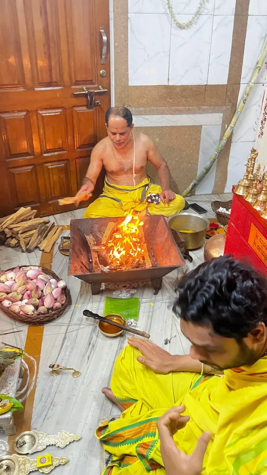 ಹಳದಿ ವಸ್ತ್ರ ಧರಿಸಿದ ಭಕ್ತರೊಬ್ಬರು ಕುಂಡದ ಬಳಿ ಪ್ರಾರ್ಥನೆಯಲ್ಲಿ ಕುಳಿತಿರುವಾಗ ಹೋಮದ ಅಗ್ನಿಗೆ ಸಮಿಧೆ ಸೇರಿಸುತ್ತಿರುವ ಅರ್ಚಕರು